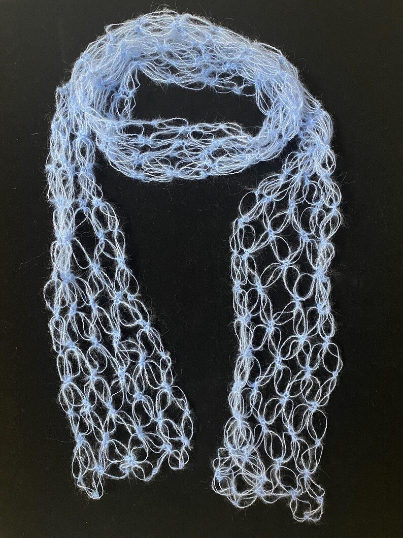 Peut inclure: Une &eacute;charpe bleu clair &agrave; tissage ouvert. L'&eacute;charpe est faite d'une mati&egrave;re douce et duveteuse et a un aspect d&eacute;licat et a&eacute;r&eacute;. Le motif pr&eacute;sente un motif r&eacute;p&eacute;titif de petites boucles interconnect&eacute;es, cr&eacute;ant un effet de dentelle. L'&eacute;charpe est pr&eacute;sent&eacute;e sur un fond sombre.