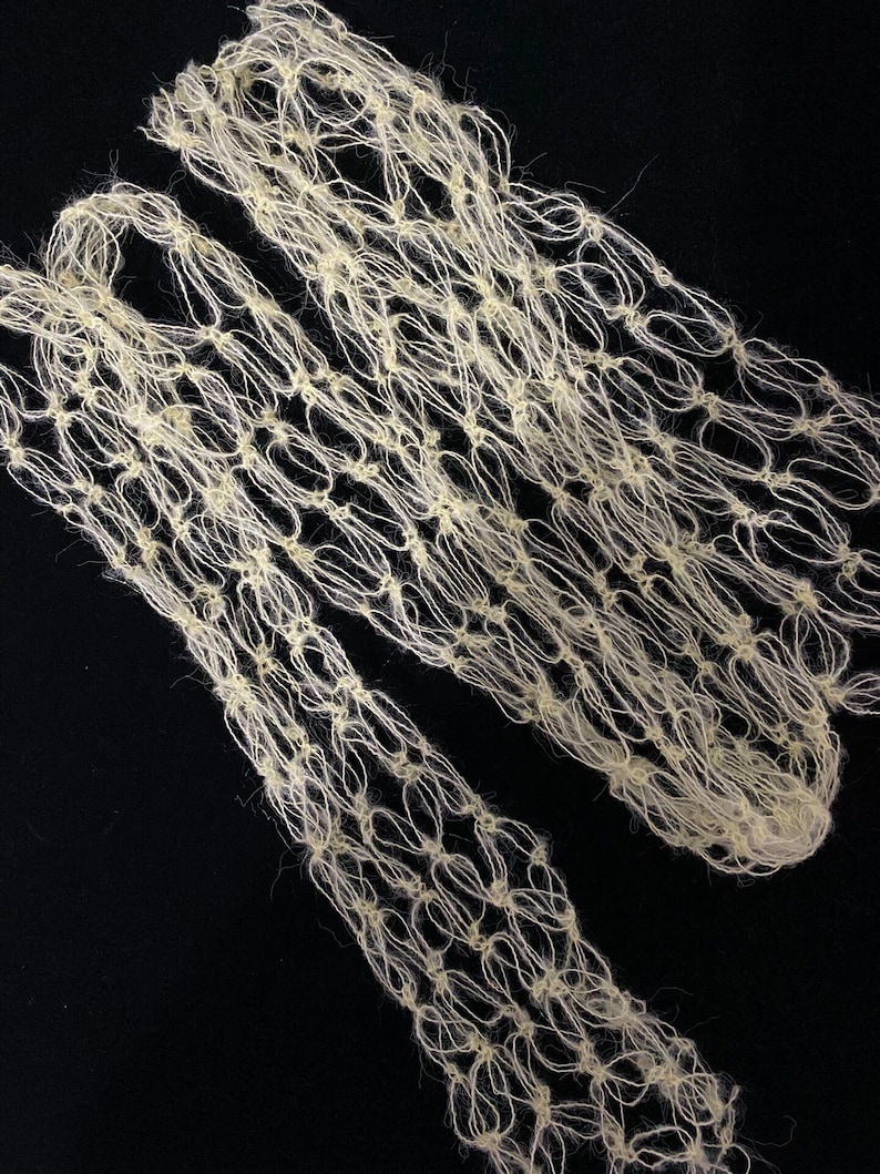 Peut inclure: Textile cr&egrave;me &agrave; tissage ouvert avec un motif en forme de filet. Le mat&eacute;riau semble &ecirc;tre fait d'un fil doux et fibreux, peut-&ecirc;tre de la laine ou une fibre naturelle similaire. Le textile est pr&eacute;sent&eacute; sur un fond noir, soulignant sa texture et son design.