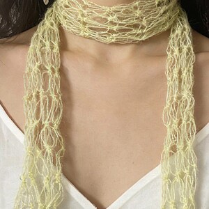 Peut inclure: Une &eacute;charpe jaune clair &agrave; tissage ouvert. L'&eacute;charpe est drap&eacute;e autour du cou et pend devant. Le mat&eacute;riau semble &ecirc;tre un fil doux et d&eacute;licat. L'&eacute;charpe est de couleur jaune p&acirc;le et a un aspect textur&eacute;. Le fond est un haut blanc.