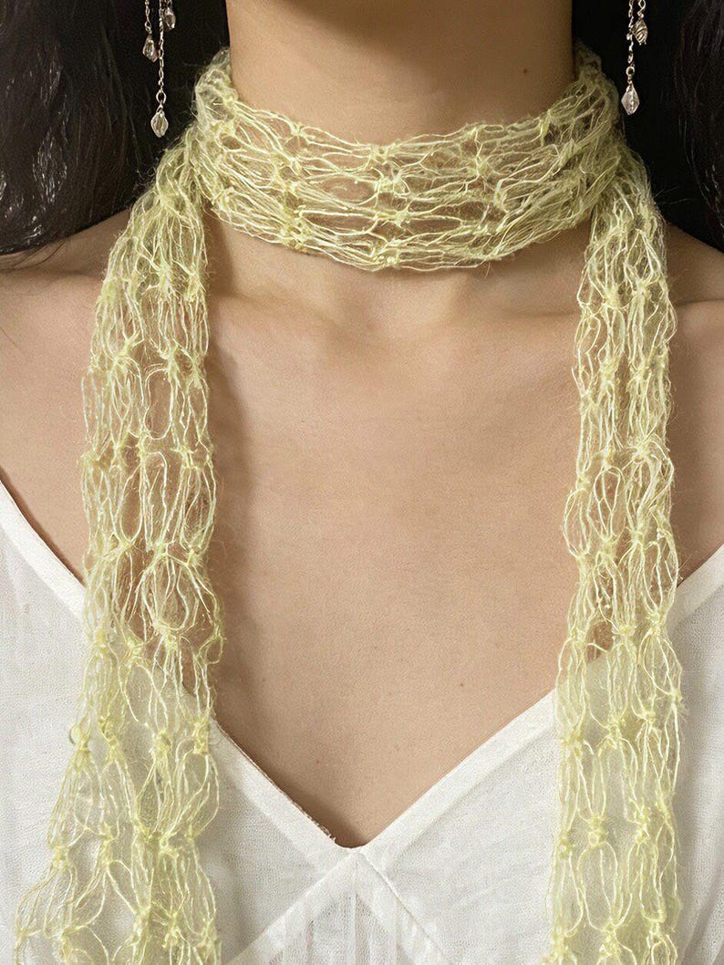 Peut inclure: Une &eacute;charpe jaune clair &agrave; tissage ouvert. L'&eacute;charpe est drap&eacute;e autour du cou et pend devant. Le mat&eacute;riau semble &ecirc;tre un fil doux et d&eacute;licat. L'&eacute;charpe est de couleur jaune p&acirc;le et a un aspect textur&eacute;. Le fond est un haut blanc.
