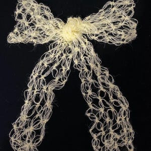 Peut inclure: Un n&oelig;ud papillon fait &agrave; la main de couleur cr&egrave;me, r&eacute;alis&eacute; en fil nou&eacute;. Le n&oelig;ud pr&eacute;sente un n&oelig;ud central et deux longues boucles fluides. Le fil a un aspect l&eacute;g&egrave;rement textur&eacute;, sur fond noir.