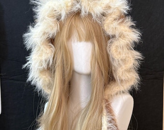 May include: A furry hood with attached ears in shades of brown and cream. The hood is made of soft, fluffy material and is designed to be worn on the head. The hood is displayed on a mannequin head with long blonde hair.