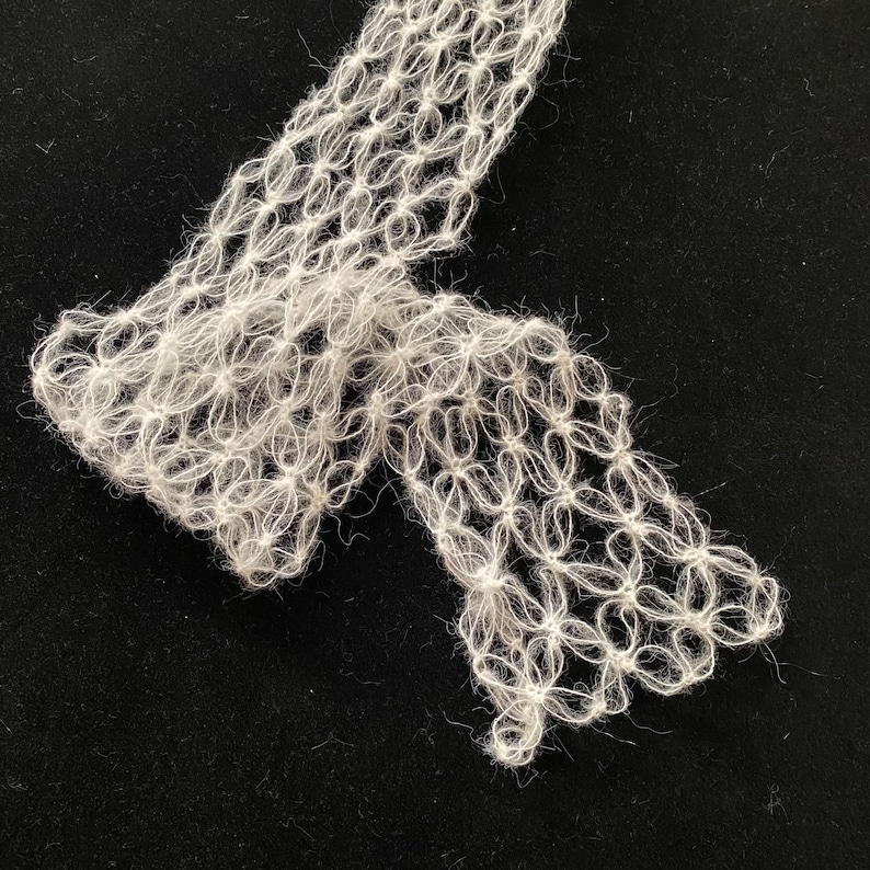 Peut inclure: Gros plan sur un textile blanc &agrave; tissage ouvert avec un motif floral. Le tissu d&eacute;licat est fait d'une mati&egrave;re douce et floue, peut-&ecirc;tre du fil ou une fibre similaire. Le textile est pr&eacute;sent&eacute; sur un fond sombre, soulignant son design complexe.