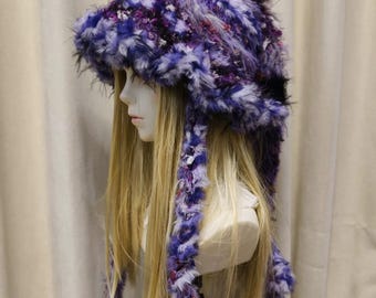 May include: A fuzzy, textured hat in shades of purple, blue, and white. The hat features a deep, shaggy pile and long, braided earflaps that hang down on either side, crafted from the same multi-colored, variegated yarn as the main cap.