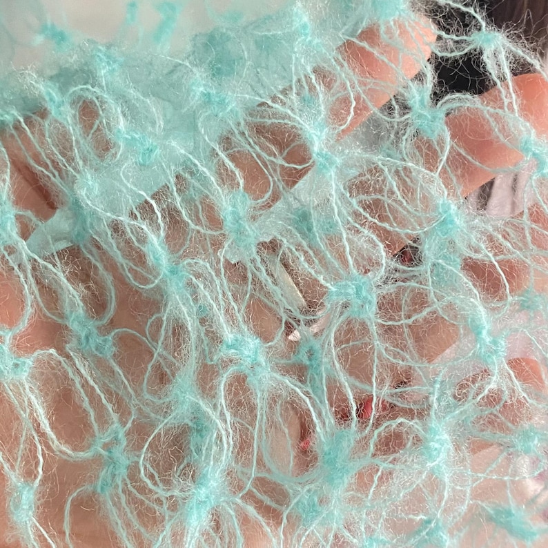 Peut inclure: Gros plan sur un tissu bleu clair &agrave; tissage ouvert. Le tissu a une structure en forme de filet avec de petits groupes touffet&eacute;s de fil aux intersections. Le fil est doux et duveteux, cr&eacute;ant un aspect d&eacute;licat et textur&eacute;. La couleur est un bleu p&acirc;le et a&eacute;r&eacute;.