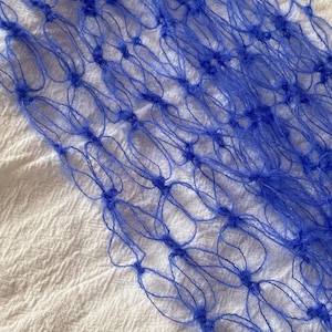Peut inclure: Gros plan sur une section de filet bleu. Le filet est fait d'un mat&eacute;riau fin et tiss&eacute;, avec un motif r&eacute;p&eacute;titif de boucles interconnect&eacute;es. Le fond est un tissu blanc textur&eacute;. Le filet est d'une couleur bleu vif.