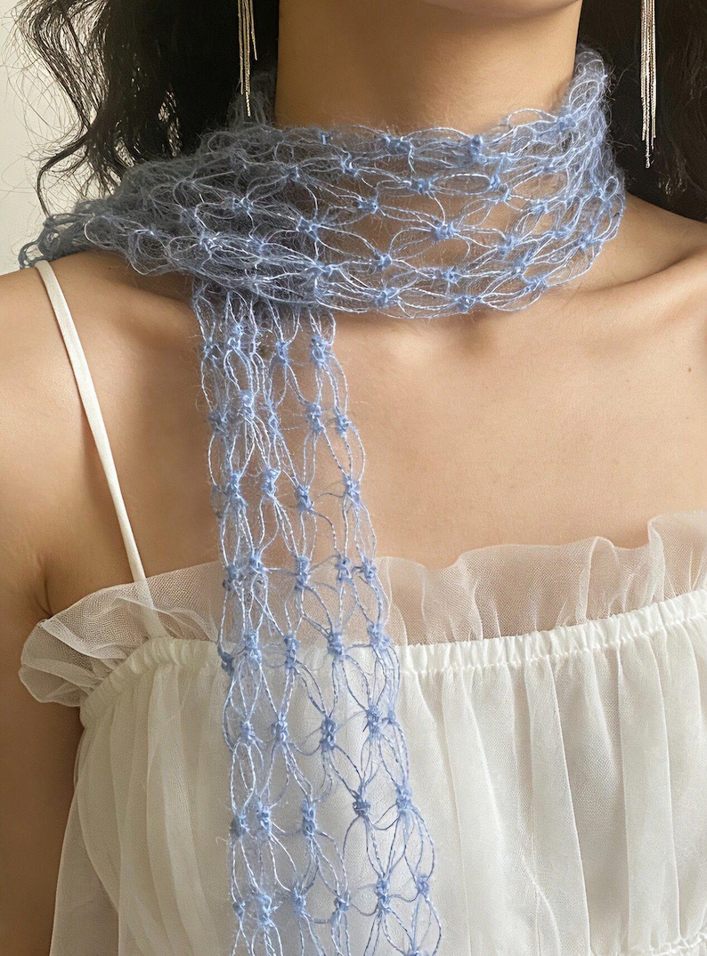 Peut inclure: Une &eacute;charpe bleu clair &agrave; tissage ouvert. L'&eacute;charpe est drap&eacute;e autour du cou et pend devant. Le design d&eacute;licat et a&eacute;r&eacute; est fait d'une mati&egrave;re douce et duveteuse. L'&eacute;charpe est port&eacute;e sur un haut blanc.