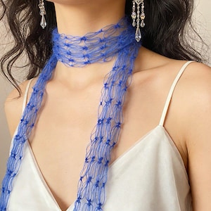 Peut inclure: Gros plan sur une &eacute;charpe bleue et des boucles d'oreilles. L'&eacute;charpe est faite d'une mati&egrave;re d&eacute;licate en forme de filet et se drape autour du cou. Les boucles d'oreilles sont argent&eacute;es avec des accents en forme de cristal. Le fond est de couleur neutre.