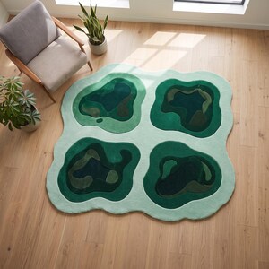 Pu&ograve; includere: Un grande tappeto dalla forma irregolare caratterizzato da una base verde menta chiaro con quattro distinti ritagli di forma organica in varie tonalit&agrave; di verde bosco, smeraldo e oliva scuro, creando un aspetto simile a una mappa topografica.