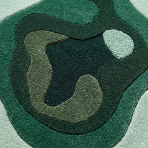 Pu&ograve; includere: Un tappeto tufted caratterizzato da una forma organica irregolare con motivi astratti a strati in varie tonalit&agrave; di verde. Il design include sezioni in verde bosco scuro, oliva e verde menta chiaro con una superficie in pelo testurizzato.