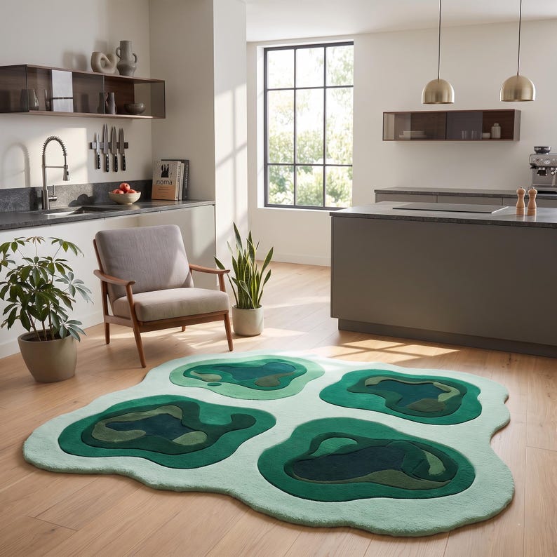 Pu&ograve; includere: Un tappeto dalla forma organica irregolare caratterizzato da un design topografico a strati in varie tonalit&agrave; di verde, che vanno dal verde menta chiaro al verde bosco scuro, creando un aspetto strutturato su un pavimento in legno chiaro.