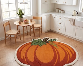 Può includere: Un grande tappeto rotondo trapuntato a forma di zucca. Il tappeto presenta un corpo color arancione vivace e ruggine scuro con un picciolo marrone scuro e una foglia verde. È delineato da un bordo spesso color crema su un pavimento in legno.