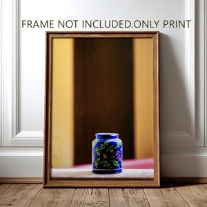 May include: A rectangular wooden frame containing a print of a blue ceramic jar with green leaves and purple flowers. The text FRAME NOT INCLUDED.ONLY PRINT is displayed above the frame. The jar sits on a surface against a blurred background.