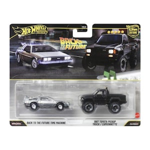 Può includere: Una confezione doppia Hot Wheels Premium contenente una macchina del tempo Back to the Future color argento e un pickup Toyota del 1987 nero. La confezione mostra il logo Back to the Future e immagini di entrambi i veicoli su sfondo scuro.