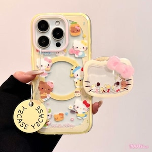 May include: Yellow phone case with a clear back and a Hello Kitty theme. The case features multiple Hello Kitty character designs, a clear ring, and a matching phone grip with a pink bow. The case has a Y2CASE tag.