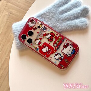 May include: A red and clear phone case with Hello Kitty designs. The case has a red border and is decorated with various Hello Kitty illustrations, including the character on a bus and holding a sign. The case is on a light blue fluffy surface.
