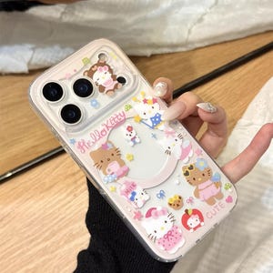 以下が含まれることがあります： 様々な衣装やアクセサリーを身につけたハローキティのキャラクターが飾られた透明な携帯電話ケース。ケースはピンクと白を基調とし、「Hello Kitty」と「Cute」の文字がデザインされています。