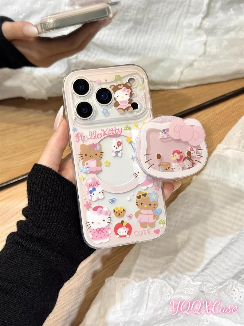 以下が含まれることがあります： ピンクのハローキティのデザインが施された透明な携帯電話ケース。ケースには、複数のハローキティのキャラクター、食べ物、そして「cute」という言葉が描かれています。ハローキティのデザインが施されたお揃いのポップソケットも表示されています。