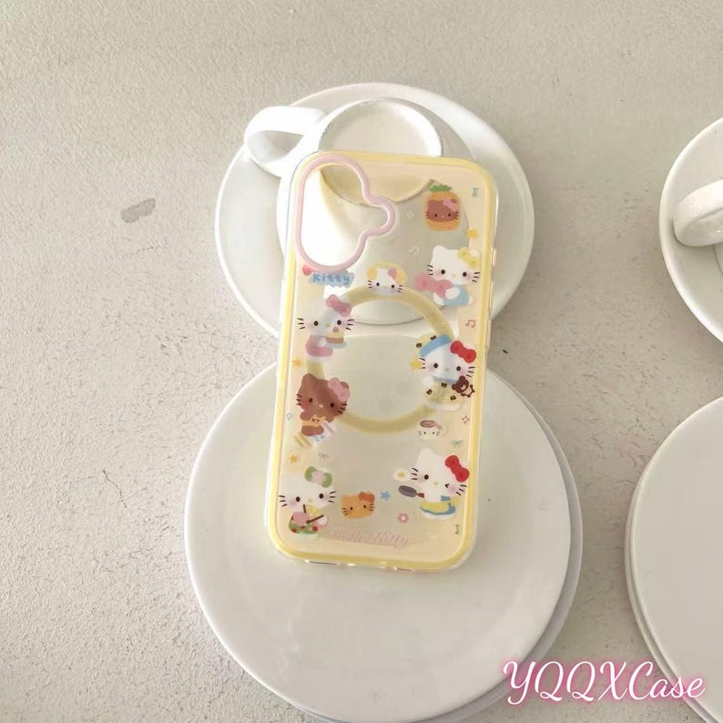 May include: A clear phone case with a yellow border and a ring for a charger. The case is decorated with multiple cartoon images of Hello Kitty. The text "YQQXCase" is visible in the bottom right corner.
