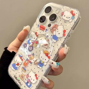 May include: Clear phone case featuring a repeating pattern of Hello Kitty characters in various poses, with red bows and blue outfits. The case has a clear border and a circular cutout for the camera.