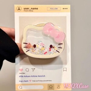 May include: A clear, Hello Kitty-shaped phone case with a pink bow and small, colorful character figures inside. The case is held in front of a social media-style background with the text "user_name From China" and "Angry Apple".