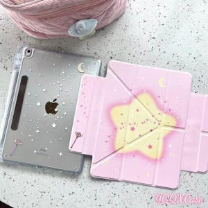 May include: A clear iPad case with a star and moon design, and a pink iPad cover with a star design. The iPad case has a pencil holder and a brown Apple logo. The pink cover has the text "YQQXCase".