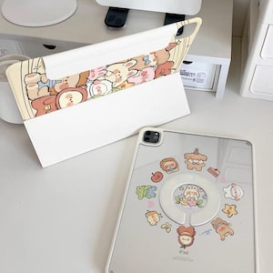 May include: A clear iPad case with a white frame and a variety of cartoon character stickers. The case is open, revealing the iPad screen. The case is on a white surface. The case has a matching cover with cartoon characters.