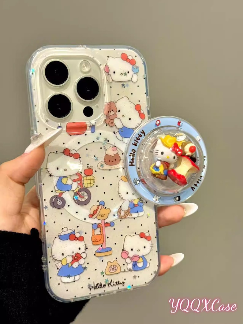 May include: Clear phone case with a Hello Kitty design. The case features multiple illustrations of Hello Kitty in various poses, with a matching pop socket. The pop socket has a blue border and a 3D Hello Kitty design. The text "Hello Kitty" is visible.