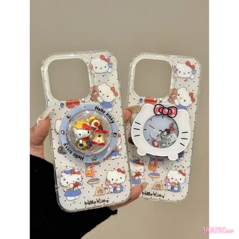 May include: Two clear phone cases featuring Hello Kitty designs. One case has a rotating charm with Hello Kitty and other figures. The other case has a white clock-shaped charm with a red bow. Both cases have a pattern of Hello Kitty characters.