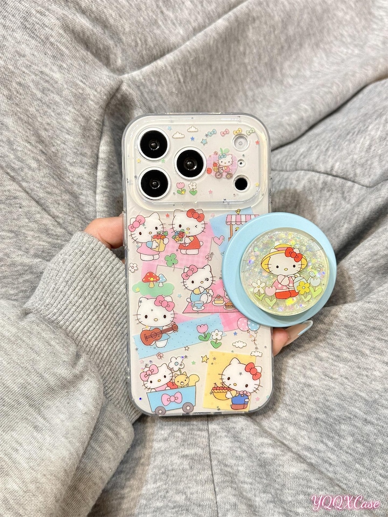 Puede incluir: Funda transparente para tel&eacute;fono con ilustraciones de Hello Kitty y un soporte popsocket azul claro. La funda tiene un fondo transparente con im&aacute;genes coloridas de Hello Kitty. El soporte popsocket tiene una base azul y una parte superior transparente con un dise&ntilde;o de Hello Kitty.