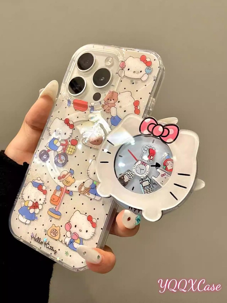May include: Clear phone case with a Hello Kitty design. The case features multiple Hello Kitty illustrations and a matching white clock accessory with a pink bow. The text "Hello Kitty" is visible on the case.