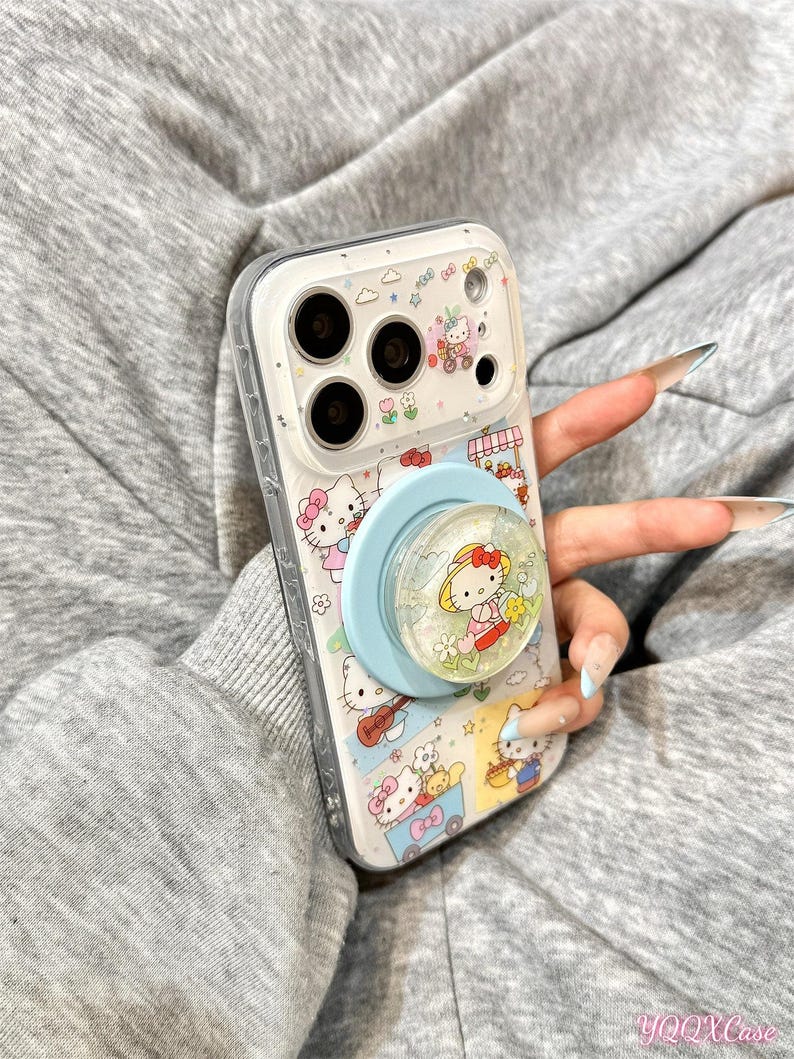 Puede incluir: Funda transparente para tel&eacute;fono con un dise&ntilde;o de Hello Kitty y un soporte emergente azul claro. La funda tiene un borde blanco y un patr&oacute;n repetido de personajes de Hello Kitty, flores y otros elementos decorativos.