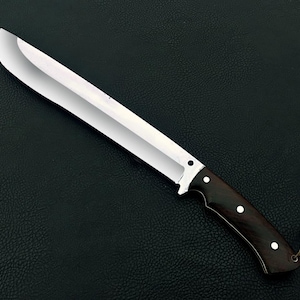 May include: A large, stainless steel knife with a dark wooden handle. The blade is wide and rectangular, with a sharp edge. The handle is dark brown with three white rivets. A leather cord is attached to the end of the handle.