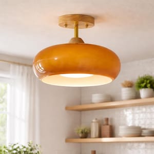 May include: A contemporary ceiling light with an amber glass shade. It's attached to the ceiling with a wooden base and a brass stem. The light is on, giving off a soft, warm glow. The light would suit a modern kitchen or living room.