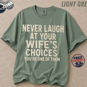 Peut inclure: Un t-shirt à manches courtes vert clair avec le texte crème NEVER LAUGH AT YOUR WIFE'S CHOICES YOU'RE ONE OF THEM imprimé en lettres grasses sans empattement sur la poitrine. Le vêtement présente un col rond et une coupe décontractée.