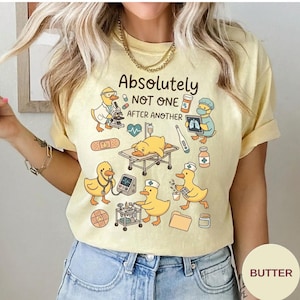 Peut inclure: Un t-shirt jaune pâle avec un motif de canards de dessin animé habillés en professionnels de santé. Le texte indique "Absolutely NOT ONE AFTER ANOTHER" entouré d'illustrations d'un microscope, d'un lit d'hôpital, d'un thermomètre et de pilules.