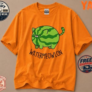 May include: An orange short-sleeve t-shirt featuring a graphic of a round, green, striped cat shaped like a watermelon. Below the cat, the text reads "WATERMEOWLON" in black letters. The shirt has a crew neckline and a standard fit design.