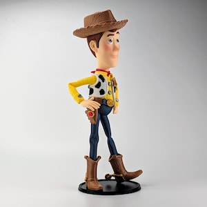 May include: A plastic figurine of a cowboy character wearing a brown textured hat, a yellow long-sleeve shirt, a white vest with black cow-print spots, a red neckerchief, a gold sheriff badge, a brown belt with a gold buckle, and blue pants.