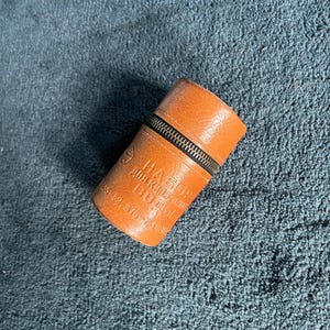Könnte beinhalten: Ein zylindrisches, hellbraunes Etui mit strukturierter Oberfläche und einem dunklen Metallreißverschluss. Die Außenseite zeigt geprägten kyrillischen Text mit der Aufschrift "НАБОР ДЛЯ КИПЯЧЕНИЯ ВОДЫ" sowie Ziffern, darunter "55 52 876 76 13".