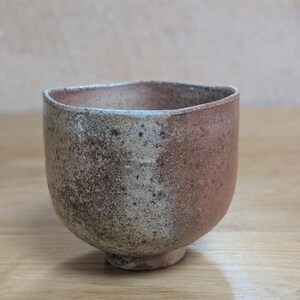 Peut inclure: Un bol en céramique fait à la main avec une forme asymétrique unique. Le bol présente un design bicolore, avec un côté clair moucheté et un côté brun rougeâtre. Le bol repose sur une petite base circulaire et a un aspect rustique et texturé.