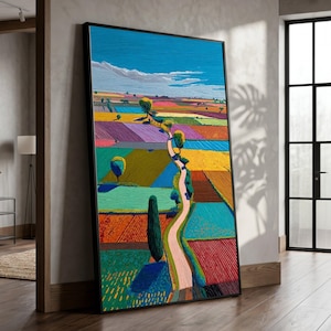 May include: A vertical framed wall art print featuring a vibrant landscape painting with a winding path through colorful patchwork fields in shades of blue, yellow, green, and red under a bright blue sky with white clouds and scattered trees.