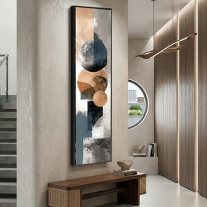 Könnte beinhalten: Vertikales abstraktes Wandbild mit geometrischen Formen und Kreisen in Blau, Braun, Grau und Schwarz. Das Kunstwerk ist in einem schwarzen Rahmen eingefasst und hängt an einer neutralfarbenen Wand. Das Thema ist modern und minimalistisch.