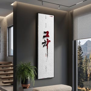 Peut inclure: Une grande œuvre d'art murale rectangulaire présentant un fond blanc texturé avec des caractères calligraphiques en coups de pinceau noirs et rouges au centre. L'œuvre est encadrée d'un fin cadre noir et comporte de petits accents de texte.