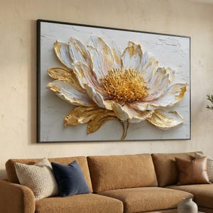 May include: A large, framed floral wall art piece. The artwork features a textured, three-dimensional flower with white, gold, and cream-colored petals. The flower's center is a textured gold, and the artwork is set against a white background.