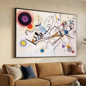 Peut inclure: Impression d'art abstrait dans un cadre noir. L'œuvre présente des formes géométriques, des lignes et des cercles de différentes couleurs, dont le noir, le blanc, le rouge, le bleu, le jaune et le violet. Le tableau est accroché au-dessus d'un canapé sectionnel marron avec des coussins décoratifs.