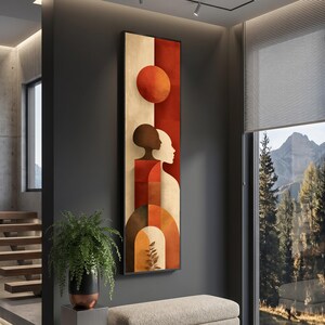 Könnte beinhalten: Vertikaler Kunstdruck mit abstraktem Design und schwarzem Rahmen. Das Kunstwerk zeigt einen orangefarbenen Kreis, einen roten und beigen Hintergrund sowie Silhouetten von zwei Figuren. Geometrische Formen und Erdtöne schaffen eine moderne Ästhetik.