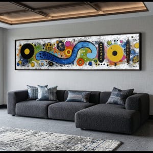 Könnte beinhalten: Ein abstraktes Gemälde mit schwarzem Rahmen hängt über einem dunkelgrauen Ecksofa. Das Kunstwerk zeigt einen weißen Hintergrund mit bunten Formen, darunter eine große blaue Wirbel, gelbe Kreise und orangefarbene Ringe. Dekorative Kissen liegen auf dem Sofa.