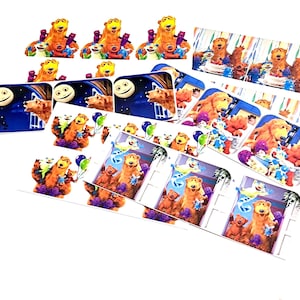 Puede incluir: Una colección de coloridas decoraciones para fiestas con el tema de Bear en la Casa Azul Grande. Las decoraciones incluyen varias formas rectangulares y troqueladas con los personajes del programa de televisión infantil. La paleta de colores incluye azules, naranjas y morados.