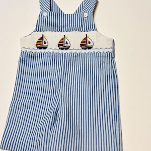 Puede incluir: Pantalones de peto para bebé de rayas azules y blancas con un babero bordado blanco con tres veleros rojos, amarillos y azules.