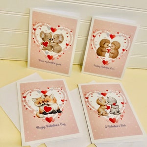 May include: Set of four Valentine's Day cards featuring animal illustrations. Each card has a pink background with a heart design and a different animal couple holding a heart. The cards include the phrases: "From my heart to yours", "Sending Valentine Love", "Happy Valentine's Day", and "A Valentine's Wish".